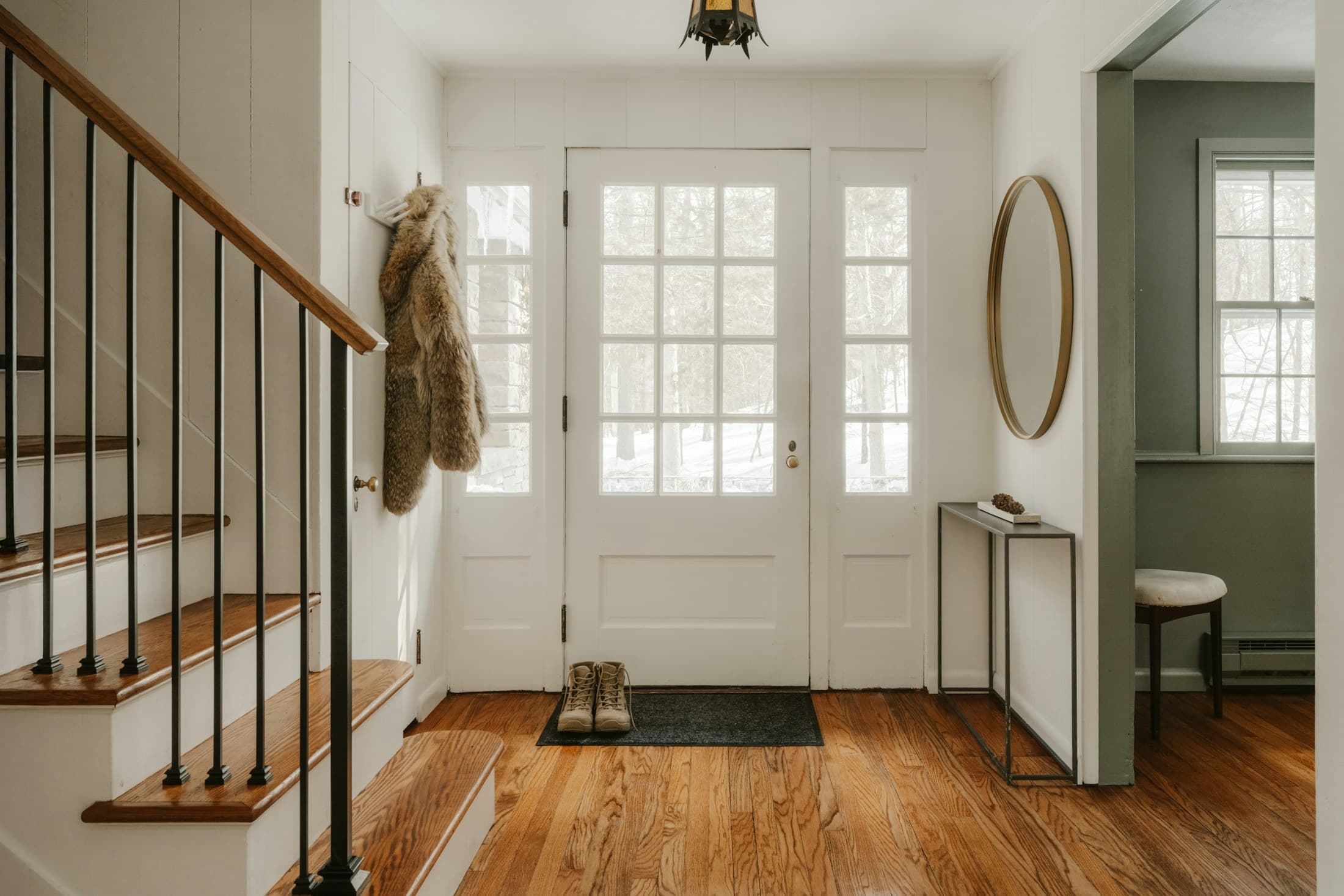 A calm entryway with wall storage, a narrow surface, mirror, and natural wood flooring.