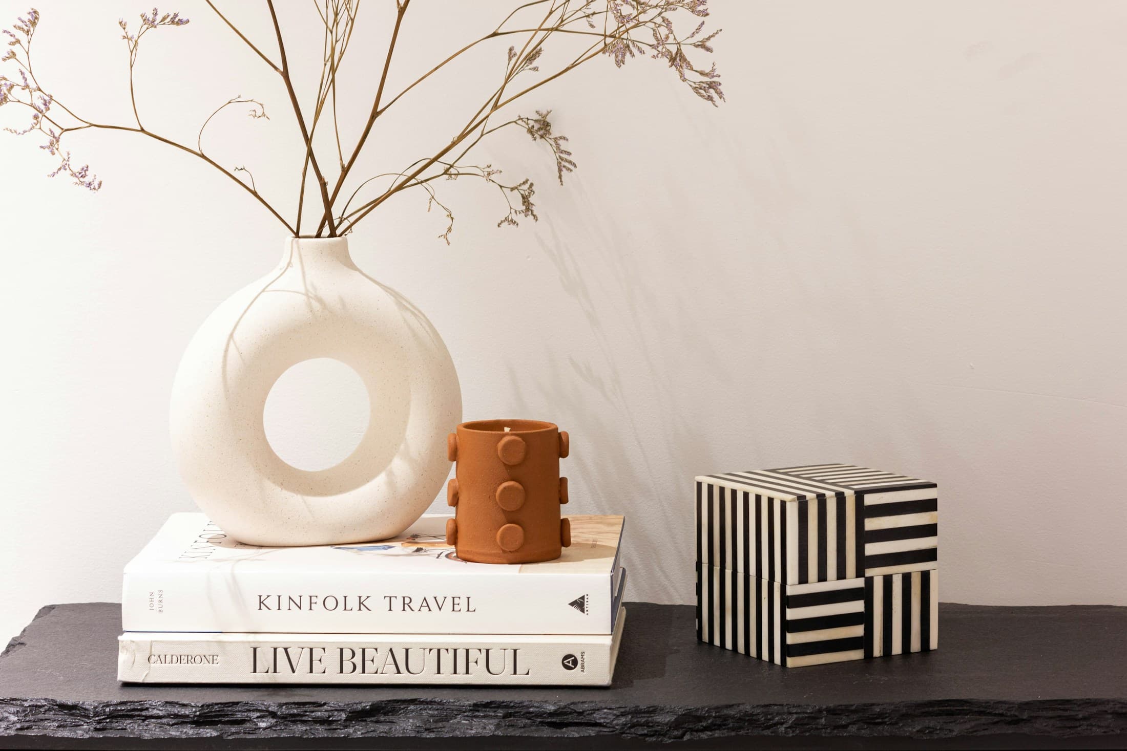 A styled studio shelf with books, a sculptural vessel, dried stems, and edited objects.
